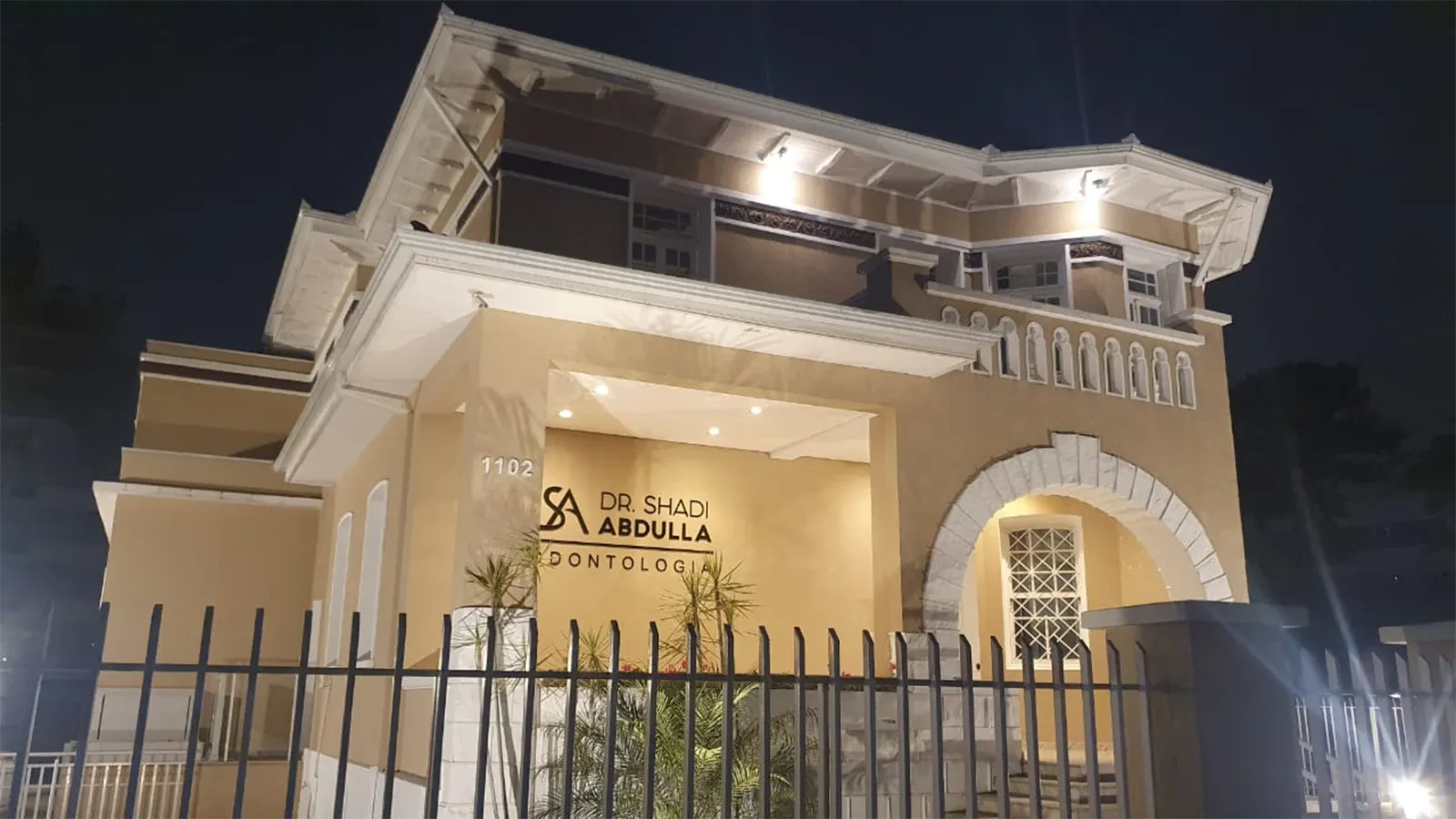 Arco de pedra, janela gradeada e grade da entrada do edifício na Av. do Batel, 1102, à noite