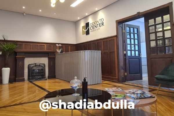 Recepção com balcão cinza canelado, painel de madeira escura, lareira, piso de tábuas e o logotipo Odonto Center Premium na parede